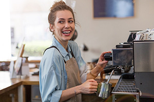 Young barista preparing coffee for customers at her cafe counter